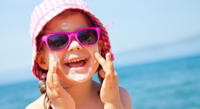 little girl wearing sunglasses, hat, and sunscreen on the beach | Sunset Vacations